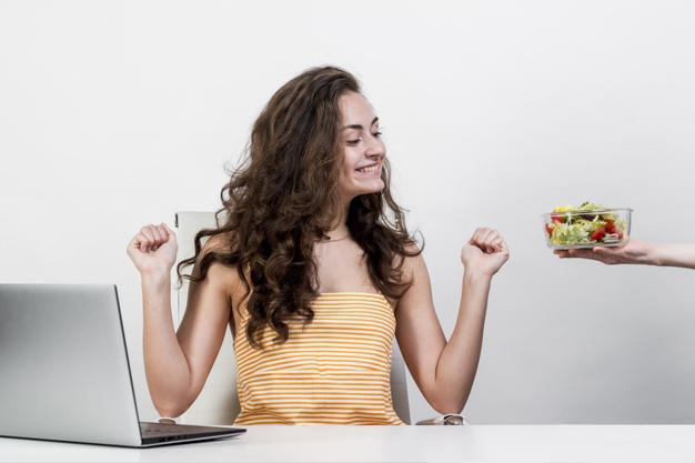 kobieta je sałatke w pracy i siedzi przy laptopie